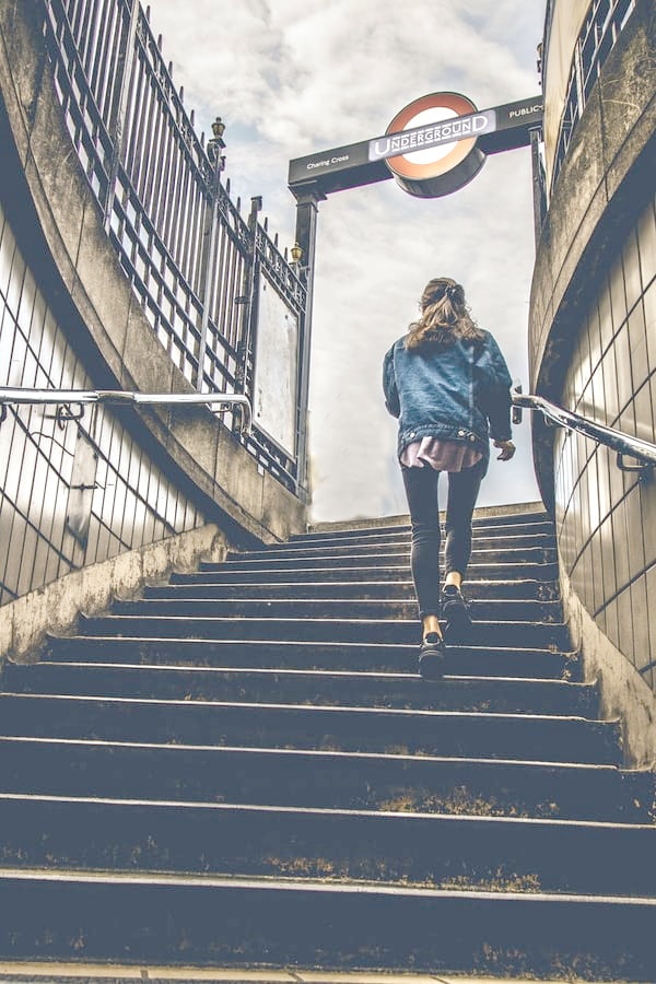 A poem by Tricia McCallum entitled Hard Won. Photo of a woman from behind climbing subway stairs.